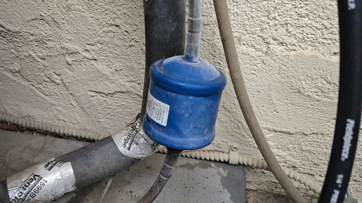 Blue filter drier on an AC liquid line beside a stucco wall, with frost on the copper line coming out of it