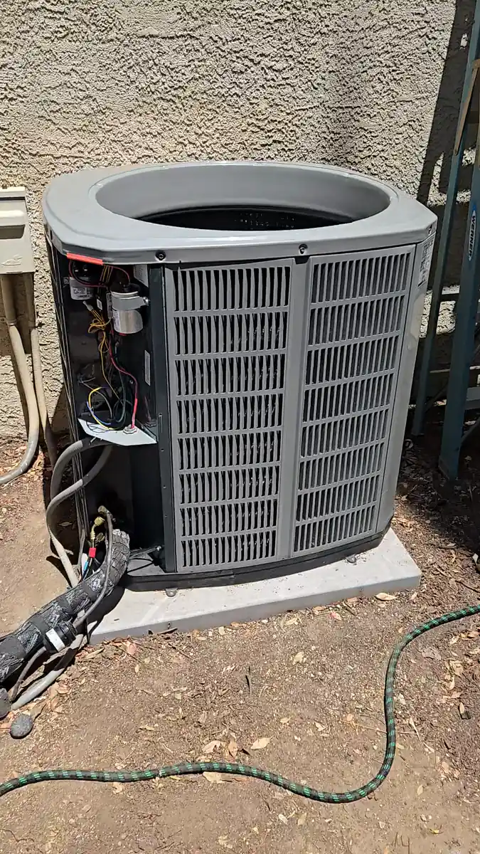 An outdoor condensing unit with the top fan grille removed and the side service panel open during a compressor replacement