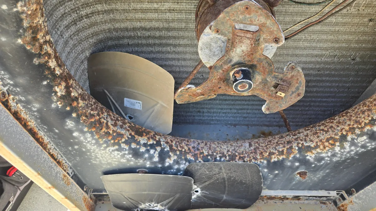 Inside a corroded Carrier side-discharge condenser: a rust-crusted fan opening, a rusted fan motor and hub, and broken fan blades lying at the bottom of the cabinet