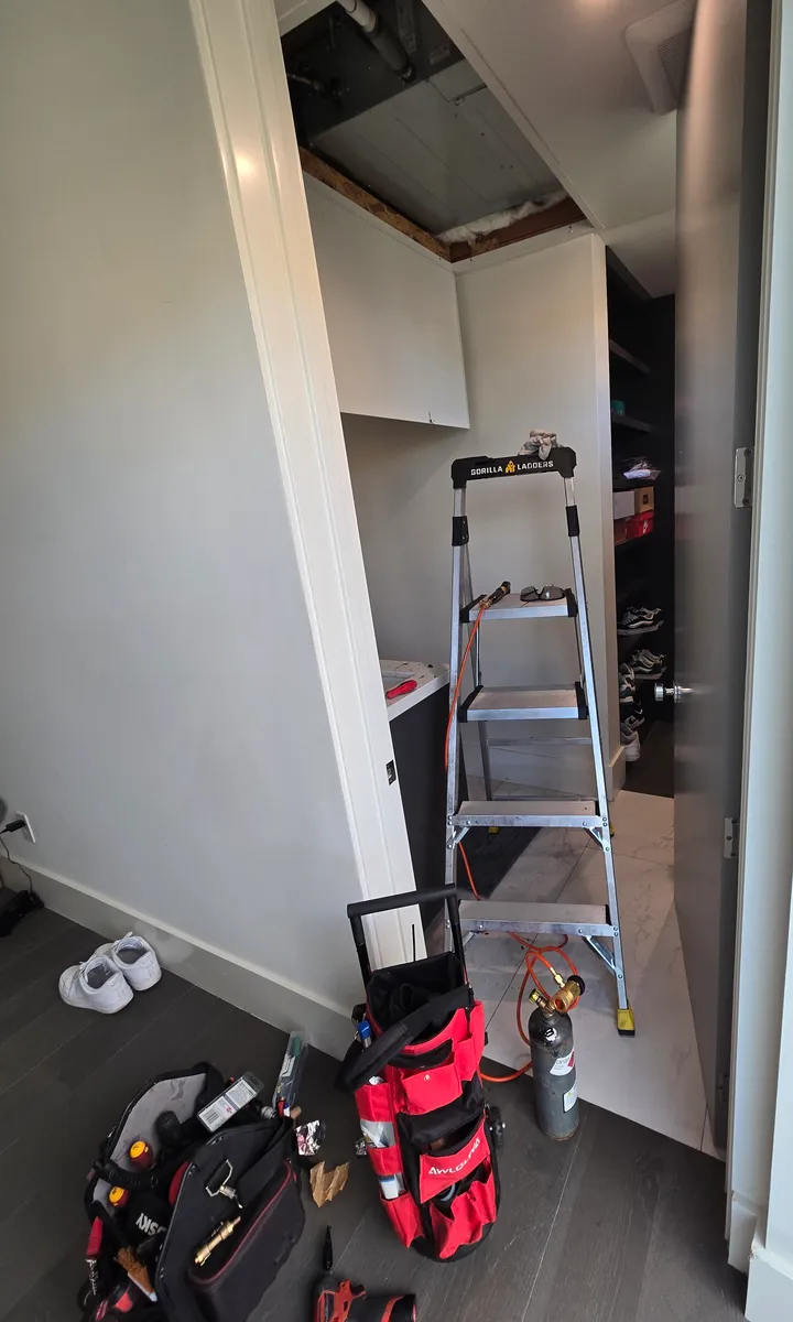 Open ceiling access panel in a hallway closet, with a step ladder below it, at a concealed mini-split air handler in a Hollywood condo