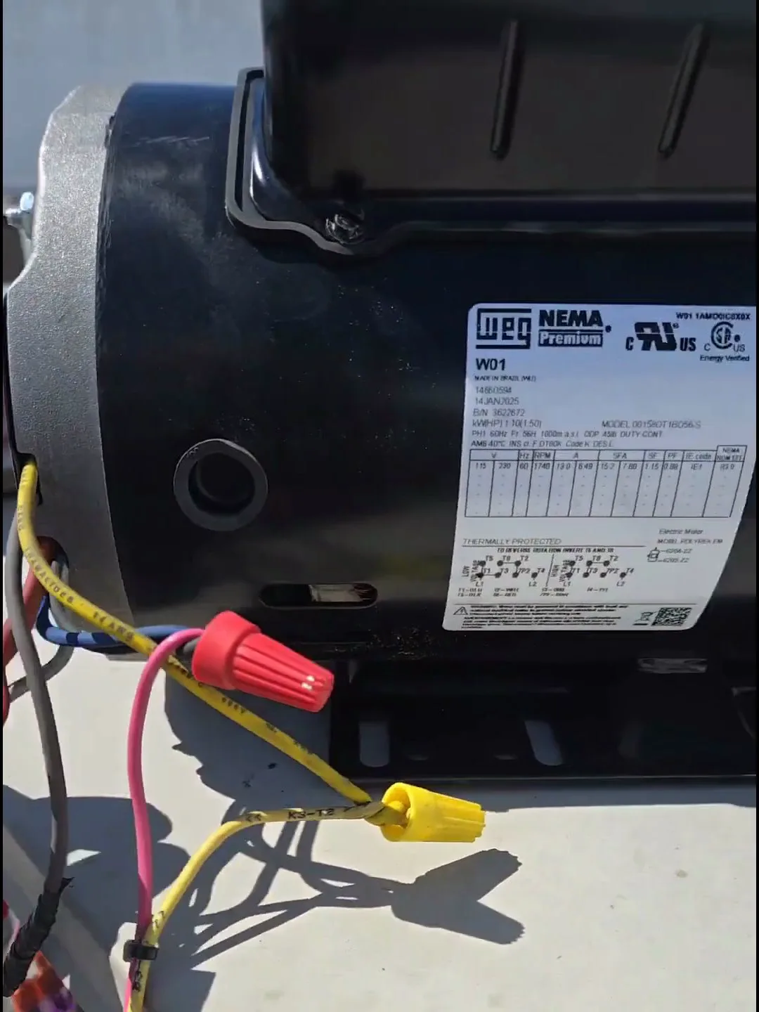 The WEG NEMA Premium replacement blower motor on the rooftop, wired up — the connection nuts follow the 115/230 V diagram that also sets rotation.
