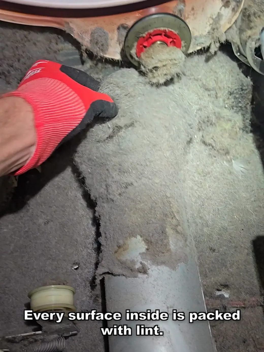 A technician's gloved hand pressing into a thick blanket of lint packed inside a dryer cabinet during a maintenance call in Los Angeles.