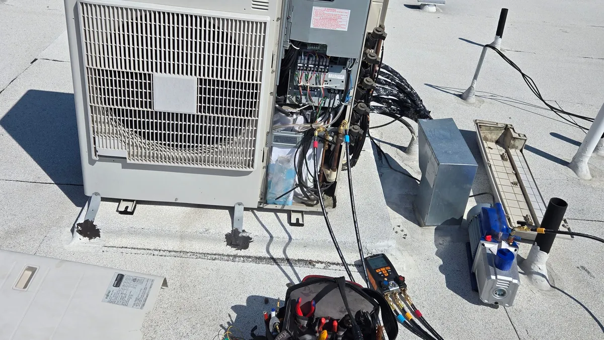 Fujitsu multi-zone outdoor unit on a flat roof, service side open, with a bundle of insulated line sets and gauge hoses connected