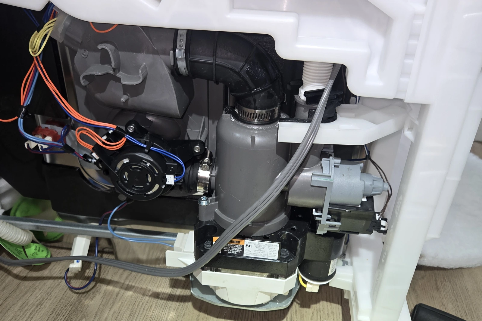 Cleaned circulation pump reinstalled on the KitchenAid dishwasher sump with new hose clamps and the drain pump mounted on the side