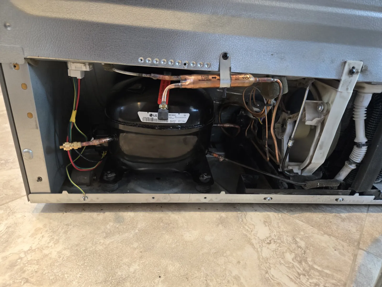 The replacement LG R134a compressor installed in an LG LFX25991ST, with a red piercing valve tapped into the line during a sealed-system repair in Los Angeles.