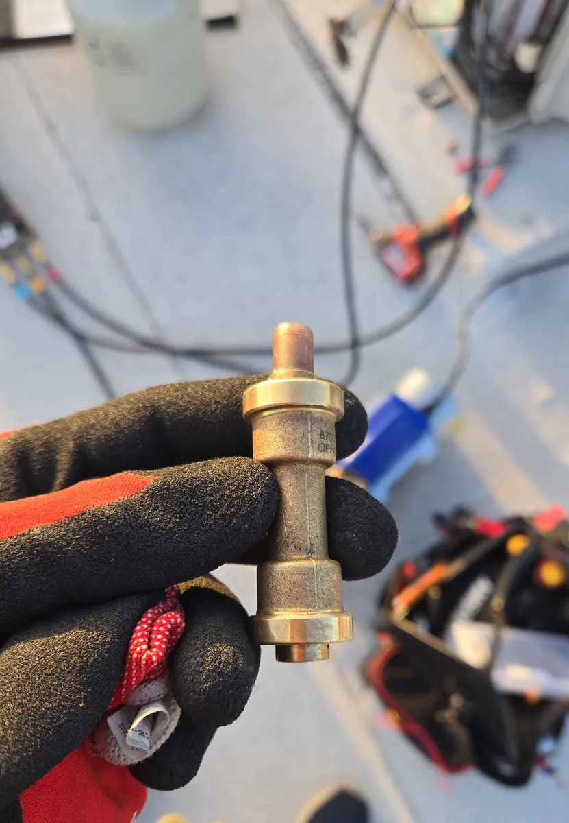 The quick-connect refrigerant fitting cut out of a ducted mini-split in a Hollywood condo, held in a gloved hand