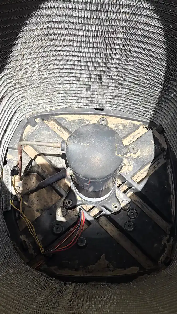 Looking down into the condenser coil at the compressor seated in the base of the unit, with its copper lines and wiring connected