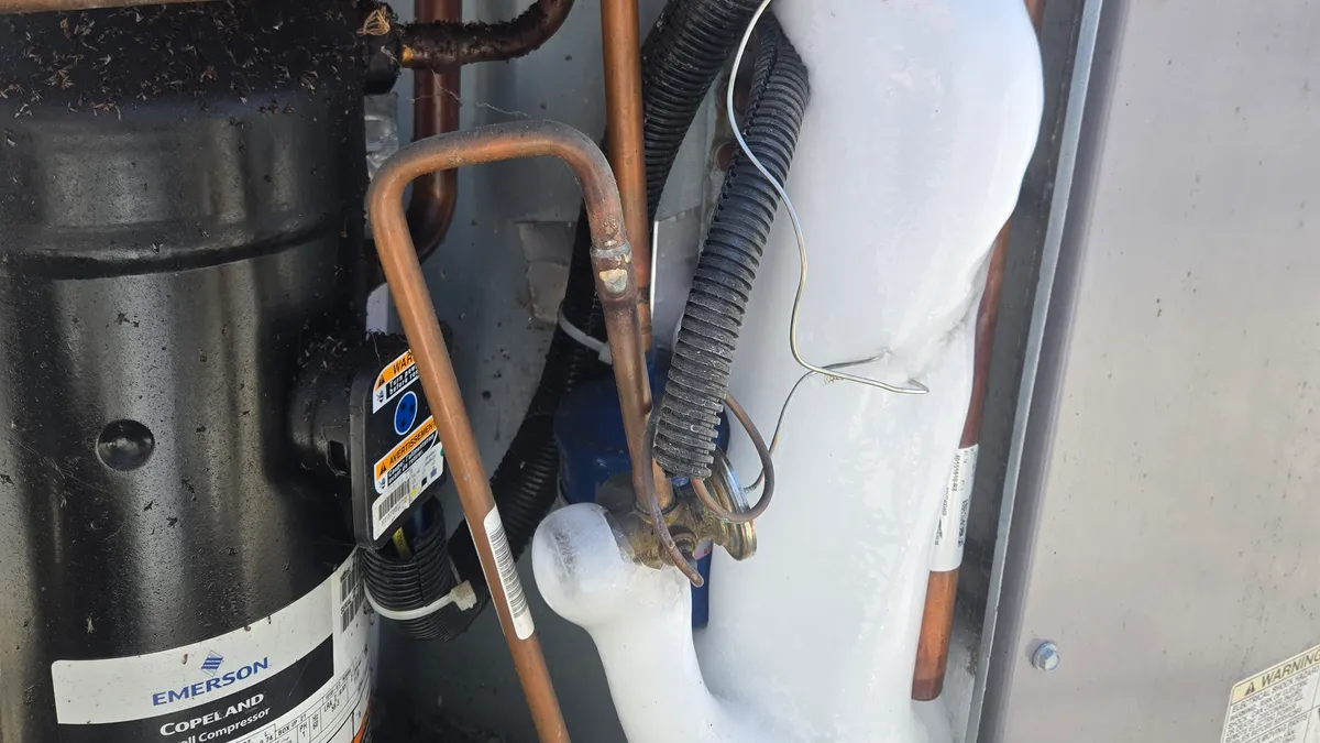 Thick white ice on the suction line beside the Copeland scroll compressor inside a packaged AC unit