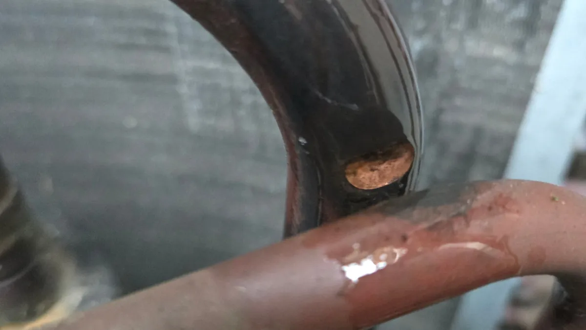 Oil-coated copper line inside an old R-22 condenser, with a bright worn spot where a smaller line crossed it and rubbed