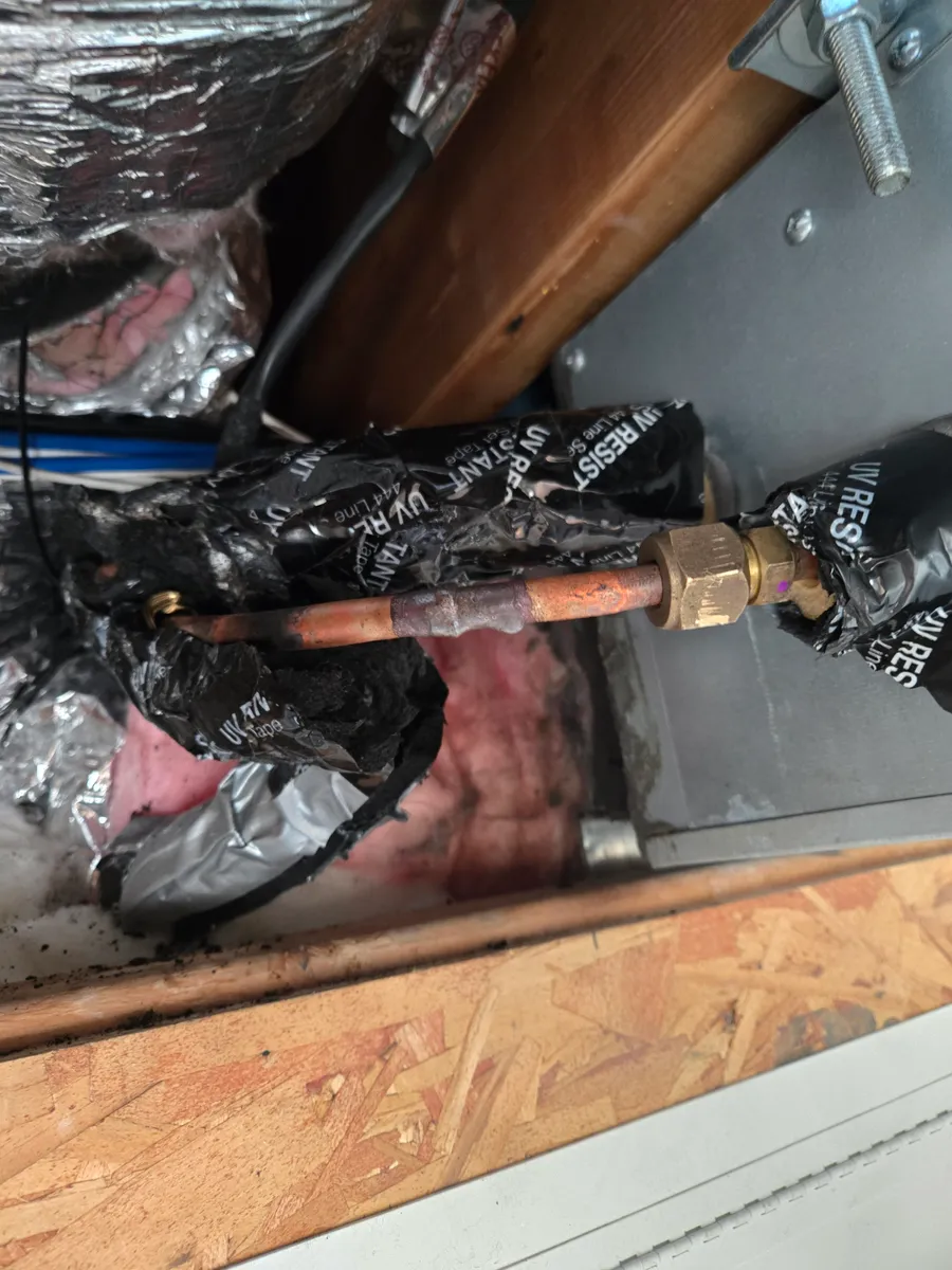 The brazed refrigerant line inside the ceiling cavity, with wood joist, OSB sheathing and fiberglass insulation on every side