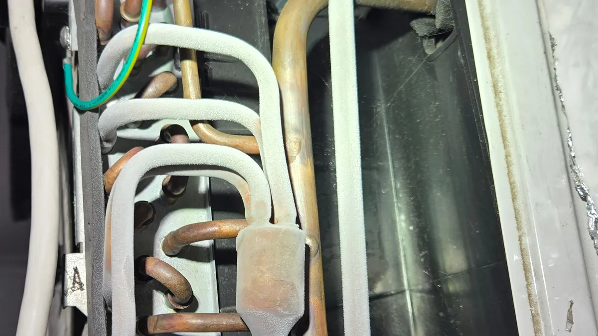 Window air conditioner with its cover off, showing copper tubes at the end of the indoor coil coated in white frost