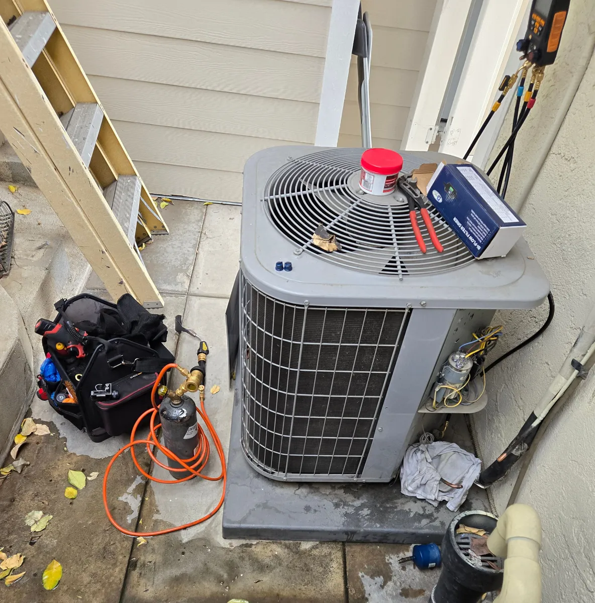 AC condenser with a new filter drier still in its box on top, a gauge manifold hooked up at right and a torch kit beside a tool bag