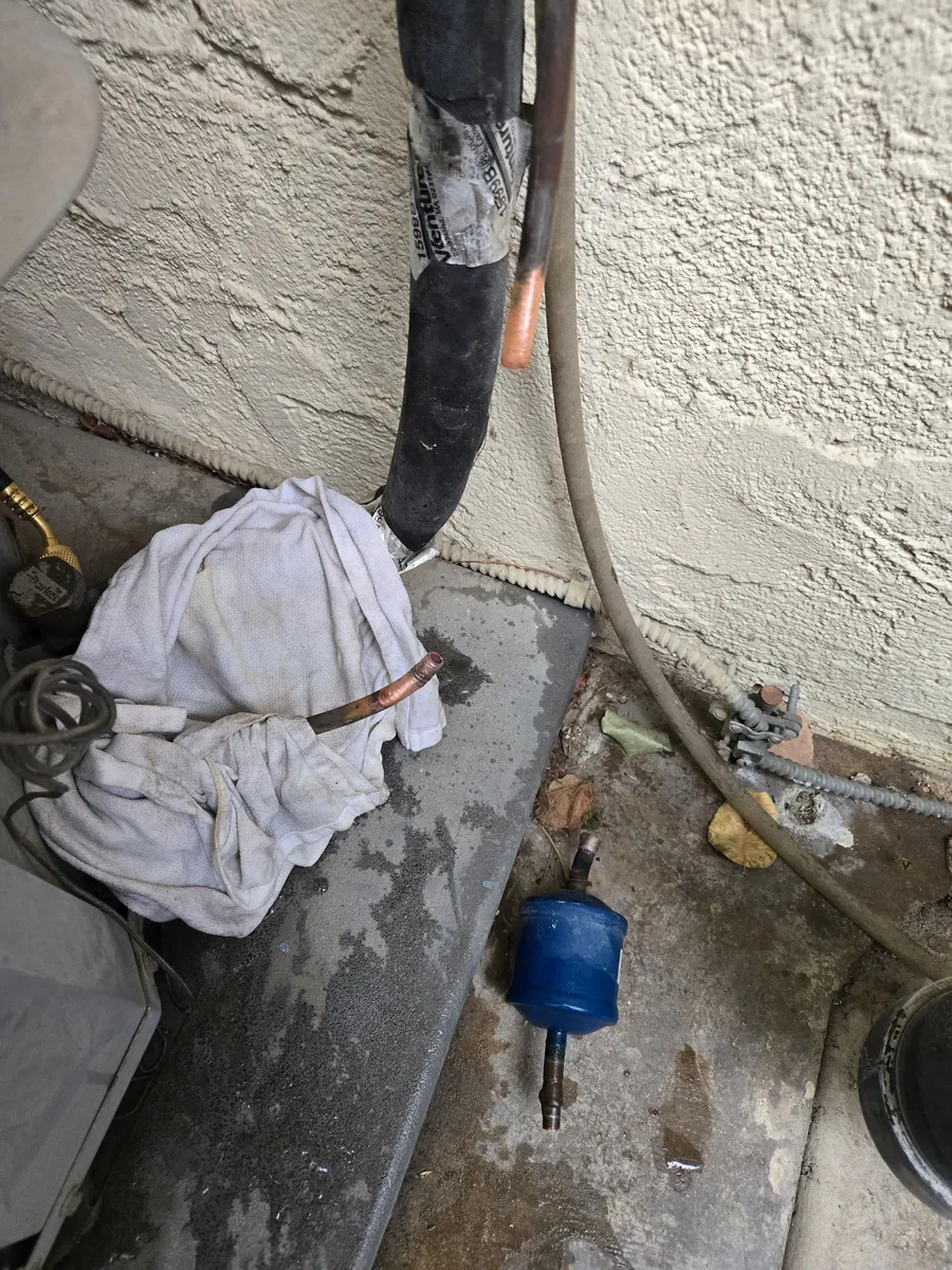 The old blue filter drier on the concrete pad after coming out of the line, with the two open ends of the copper liquid line beside the outdoor unit