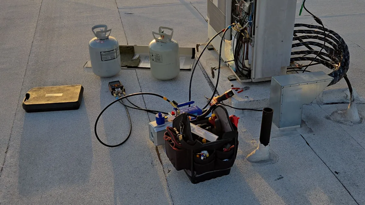 A Beverly Hills roof at sunset: two white cylinders, a digital manifold, a vacuum pump and an open tool bag, with the outdoor unit and a coil of line set behind them