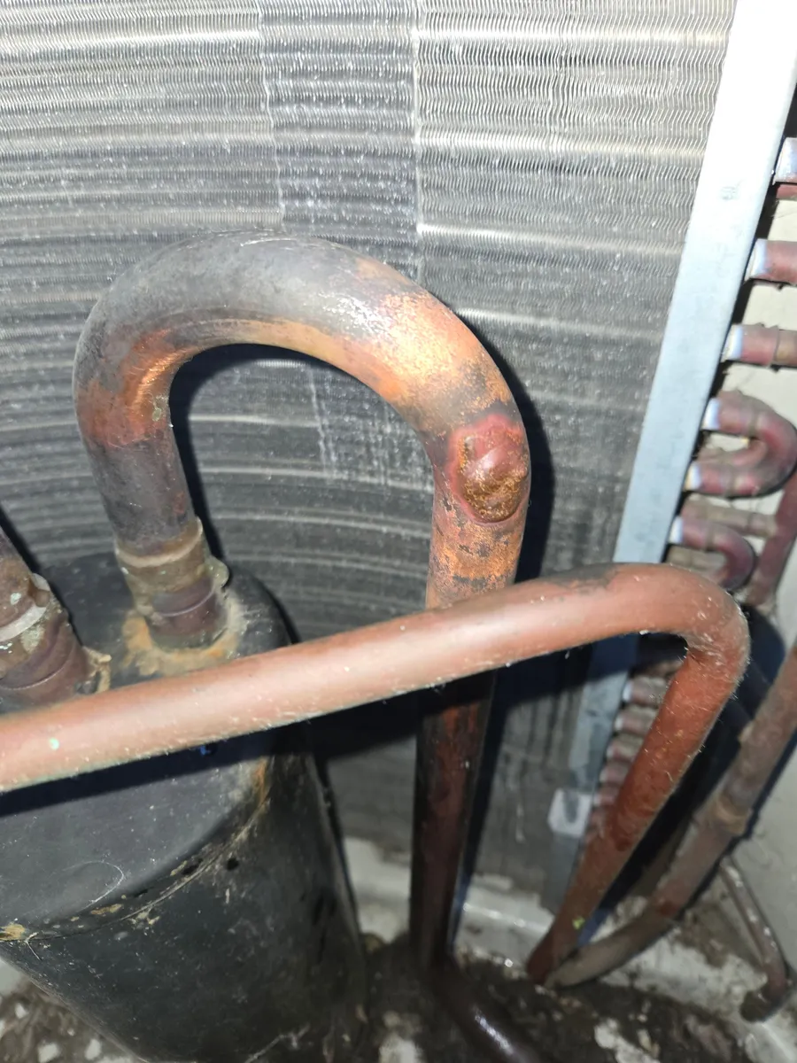 The same copper bend inside the condenser after the repair, with a brazed patch over the spot where the two lines had rubbed