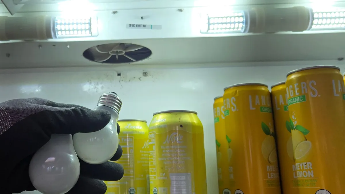 Two frosted screw-in light bulbs in a gloved hand inside a Sub-Zero refrigerator, with the lights on above them