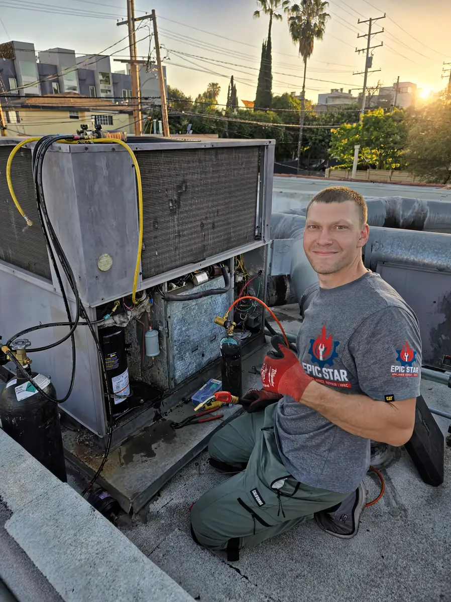 Epic Star owner-technician kneeling on a rooftop at sunset next to a commercial packaged HVAC unit with refrigerant gauges in Hancock Park, Los Angeles