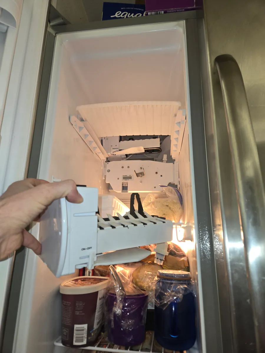 Ice maker held in front of its mount at the top of a Whirlpool side-by-side freezer