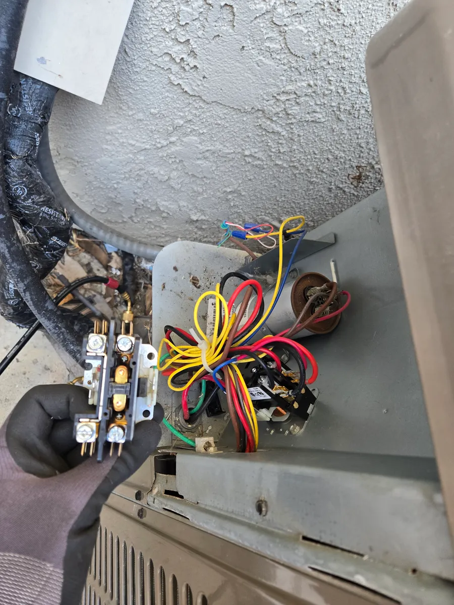 Burnt contactor held next to the open electrical compartment of a York AC condenser